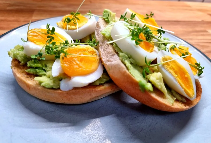 Avocado bagel topped with soft-boiled eggs and fresh microgreens